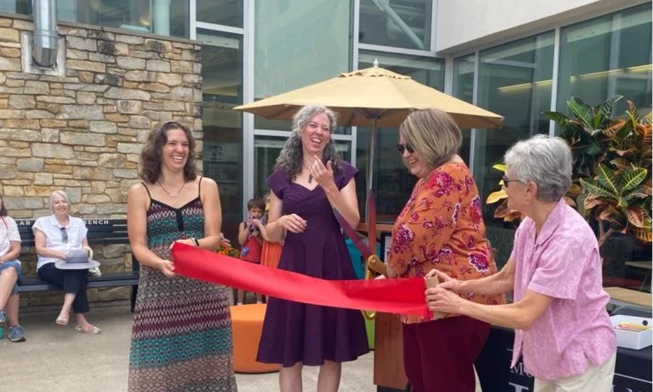 Photo of four women cutting a red ribbon with giant scissors.